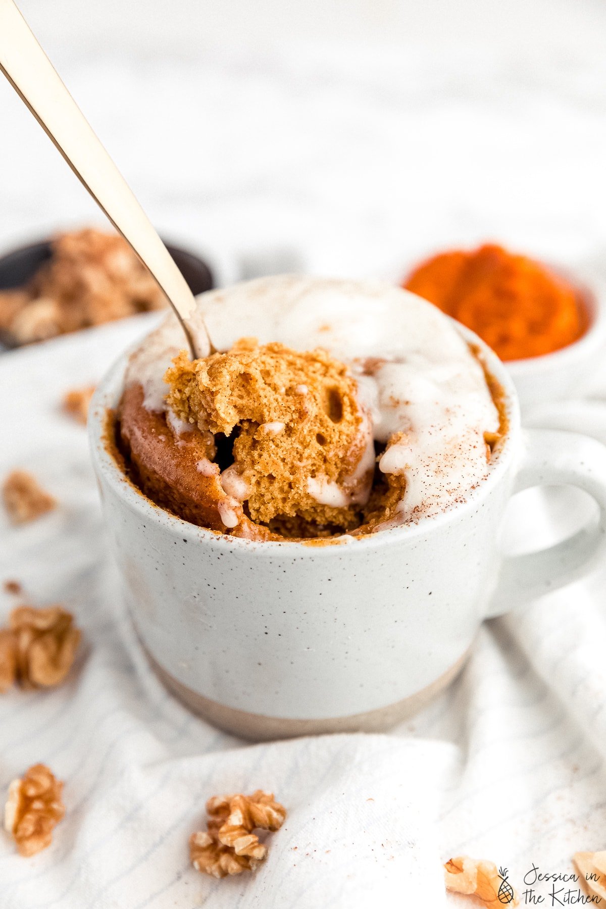 Gold spoon being pushed into and scooping out a piece of pumpkin cake out of a mug..