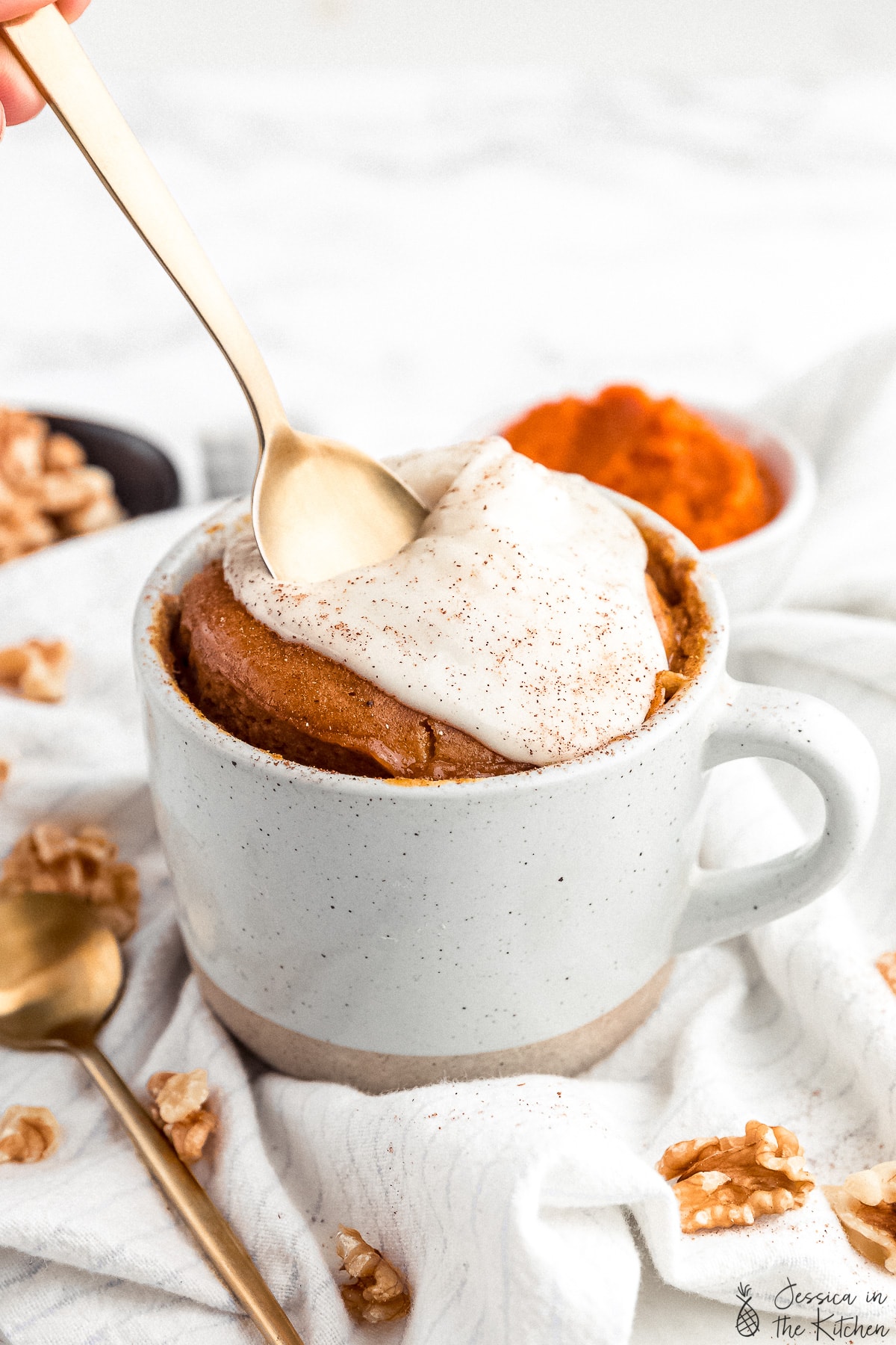 Gold spoon being pushed into a pumpkin mug cake with frosting.