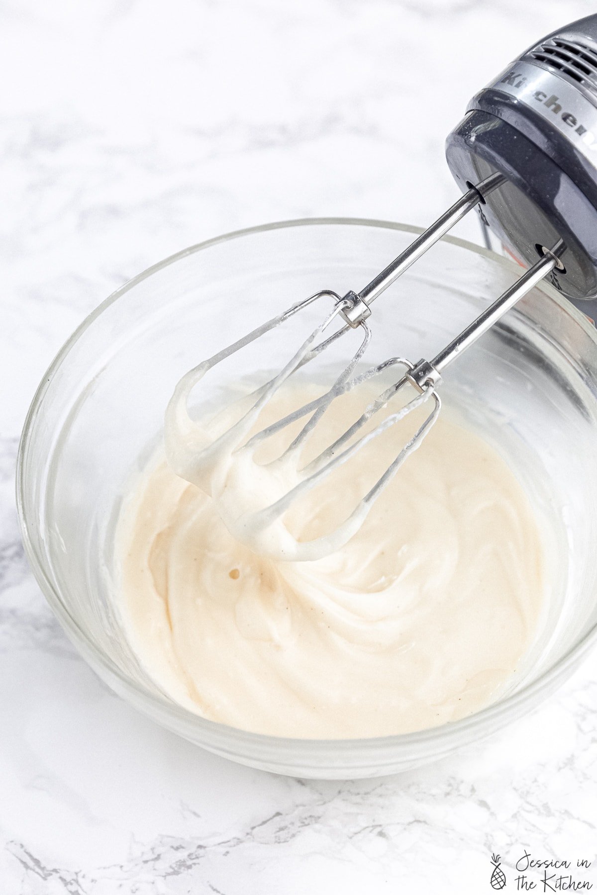 Frosting in a glass bowl with hand mixer scooping some out.