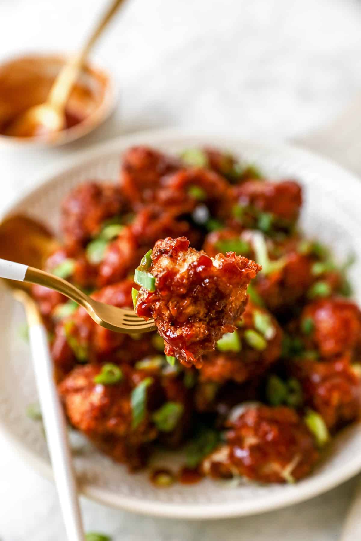 Close up of a bbq cauliflower wing on a fork with a plate of cauliflower wings in the background.