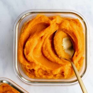 cooked pumpkin puree in a glass container with a spoon in it