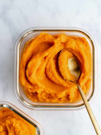 cooked pumpkin puree in a glass container with a spoon in it