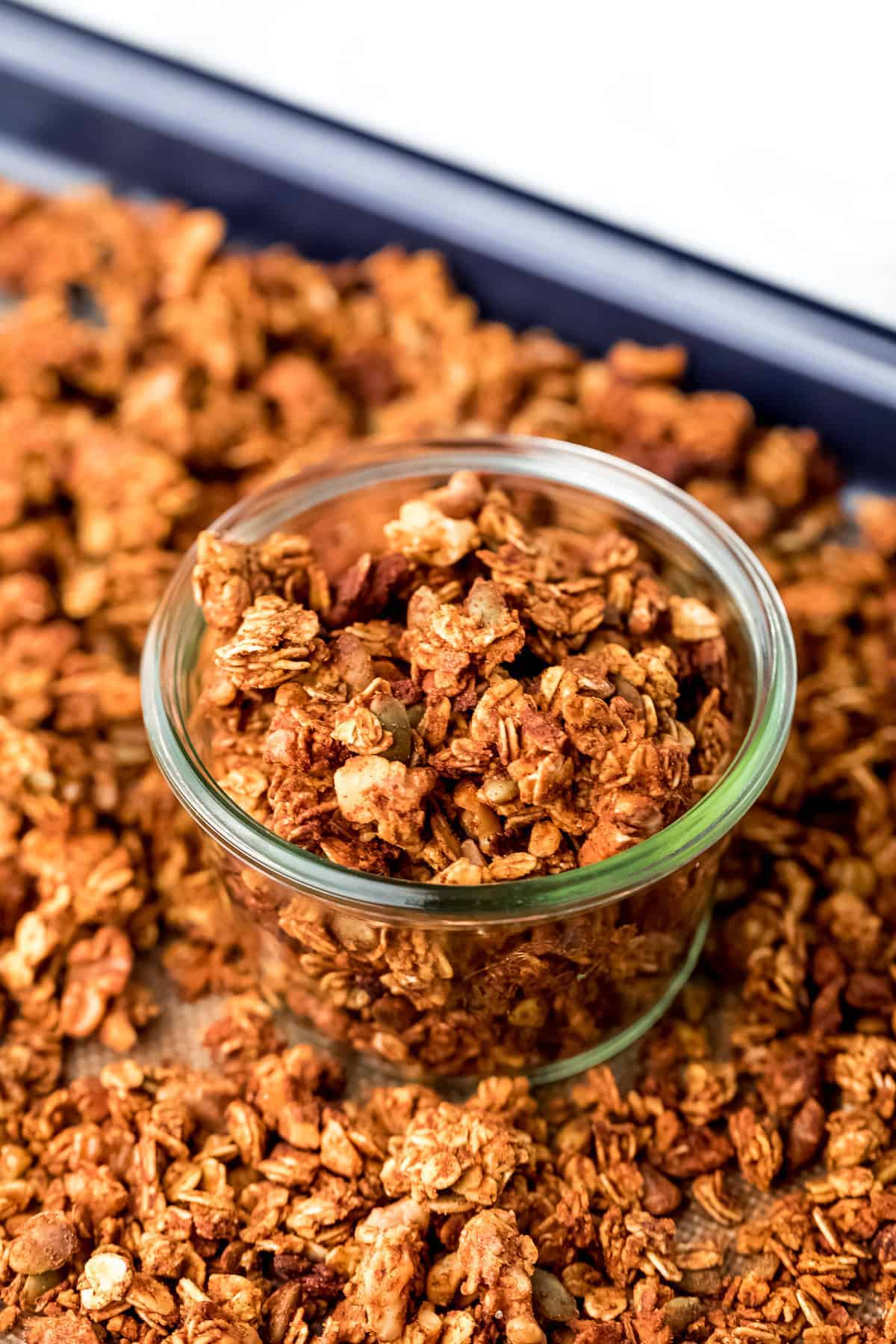 Granola in a glass jar on a baking sheet surrounded by granola.
