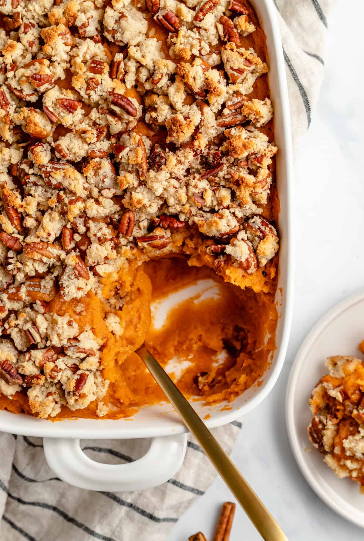 Spoon in sweet potato casserole with a scoop taken out in a plate in the corner.