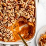 spoon in sweet potato casserole with a scoop taken out in a plate in the corner