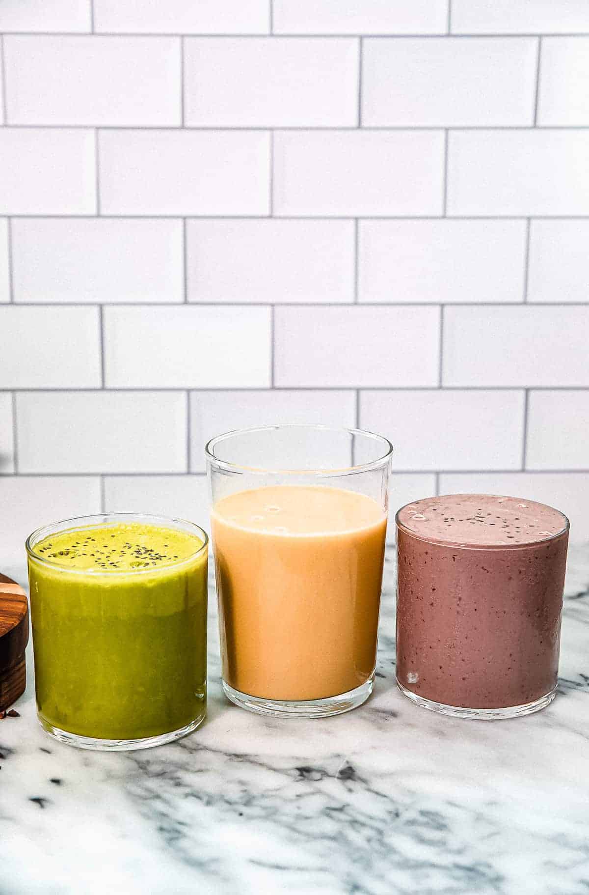 three smoothies green orange and purple on a marble countertop