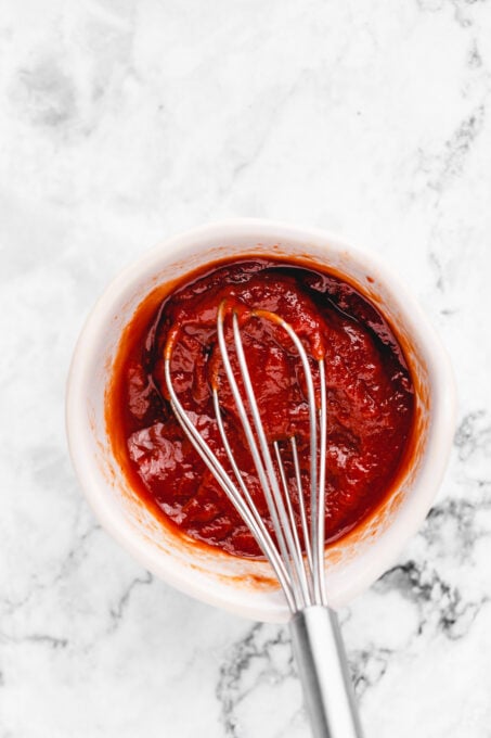 Overhead view of vegan meatloaf sauce in a bowl with a whisk.