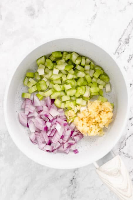 Diced red onion, garlic, and celery added to a pan.