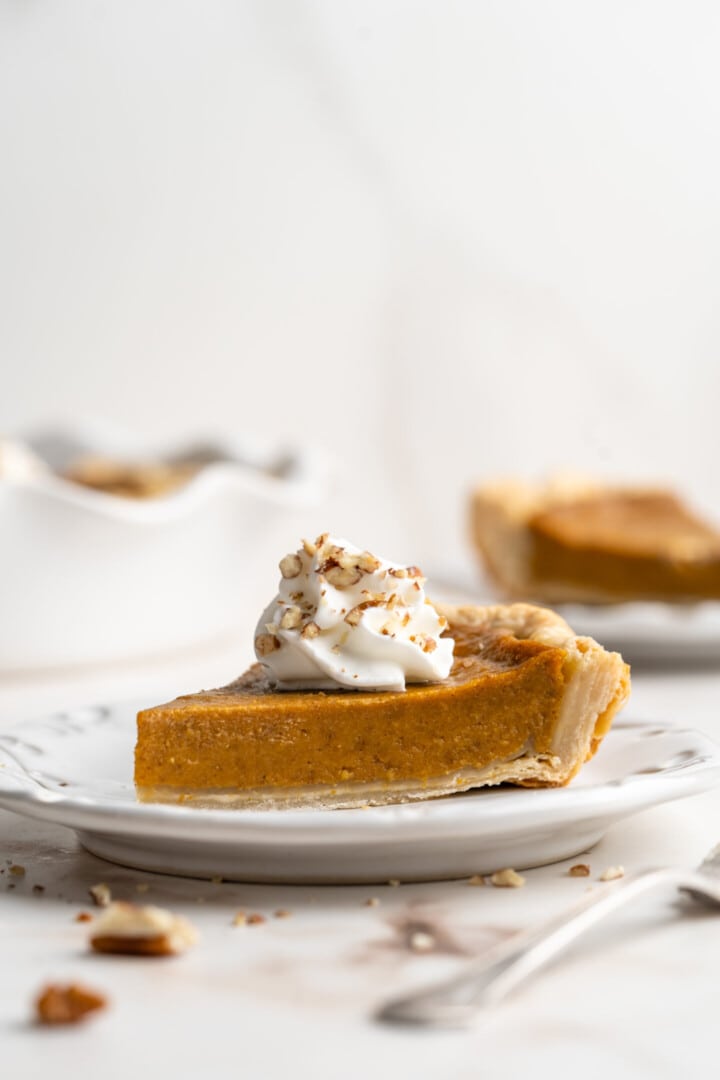 A slice of pumpkin pie with cream on top.