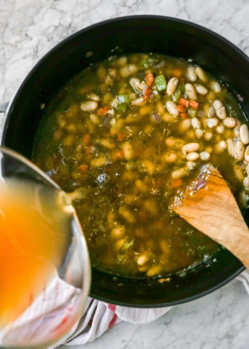 This hearty vegan white bean soup recipe is creamy and richly flavoured, perfect for keeping you warm and cozy. Only 15 minutes of prep time! pouring vegetable broth into the soup
