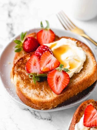 French toast with whipped cream, maple syrup, and strawberries.