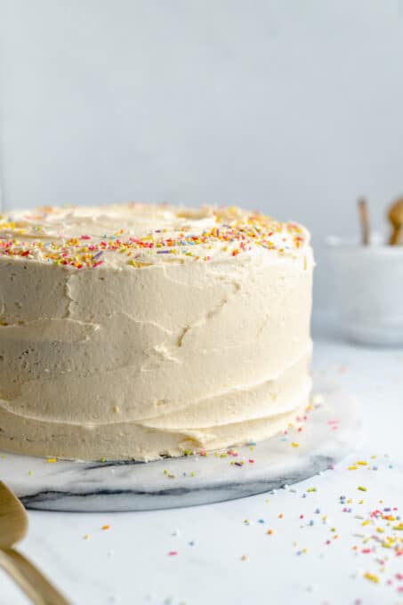 This vegan vanilla cake with buttercream frosting is light, fluffy, and delicious. It's the perfect cake for birthdays, holidays, and more! Frosted vanilla cake with sprinkles.