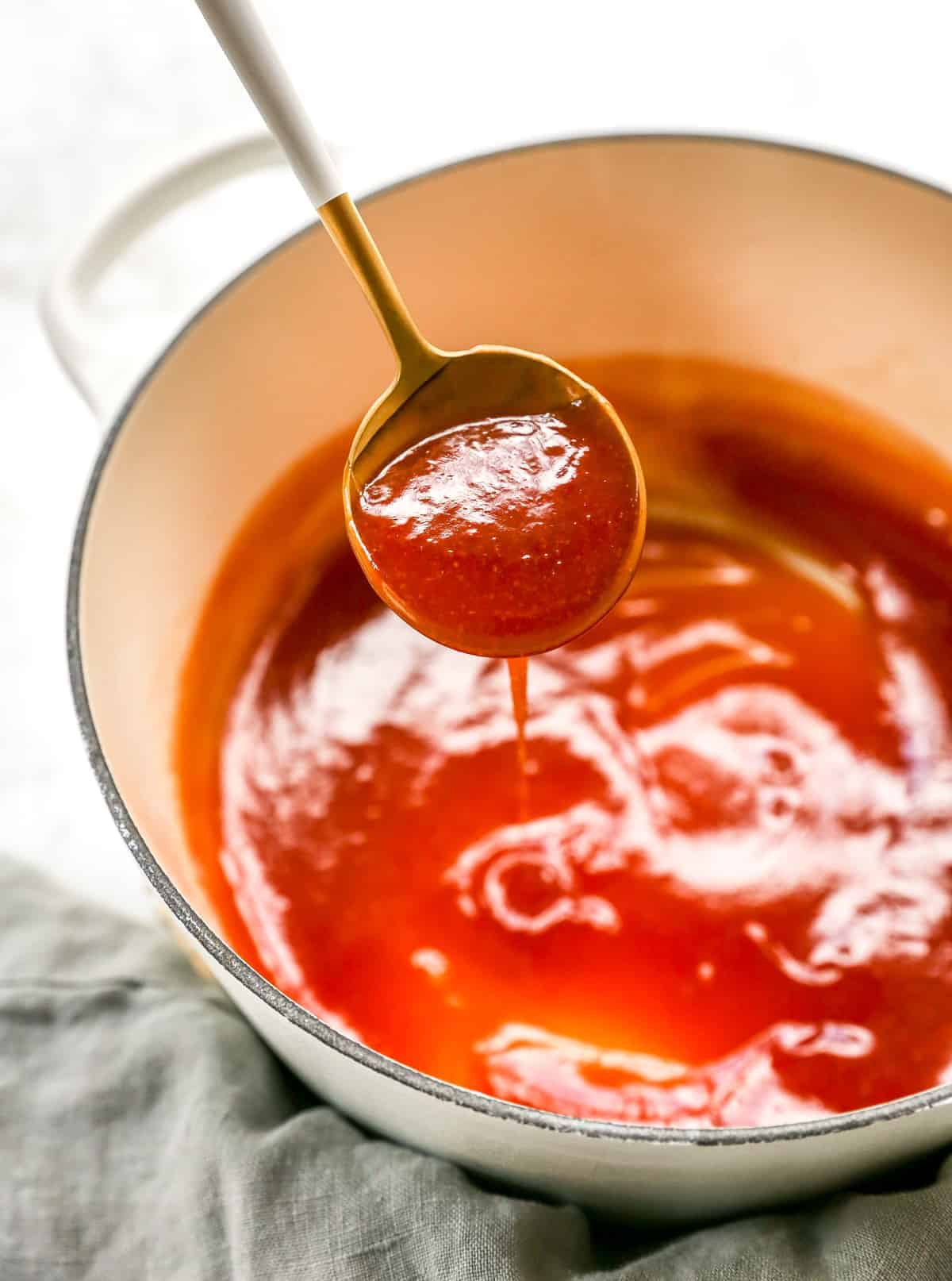 a spoon of sweet and sour sauce over pan of more sweet and sour sauce