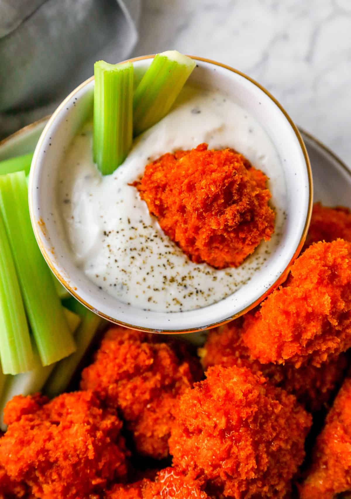 cauliflower wing dipped into a ranch dressing with celery on a plate 