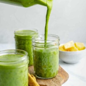 green smoothie being poured into a mason jar, surrounded by two other jars of smoothies