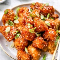 Sweet and Sour cauliflower wings piled on white plate beside gold forks