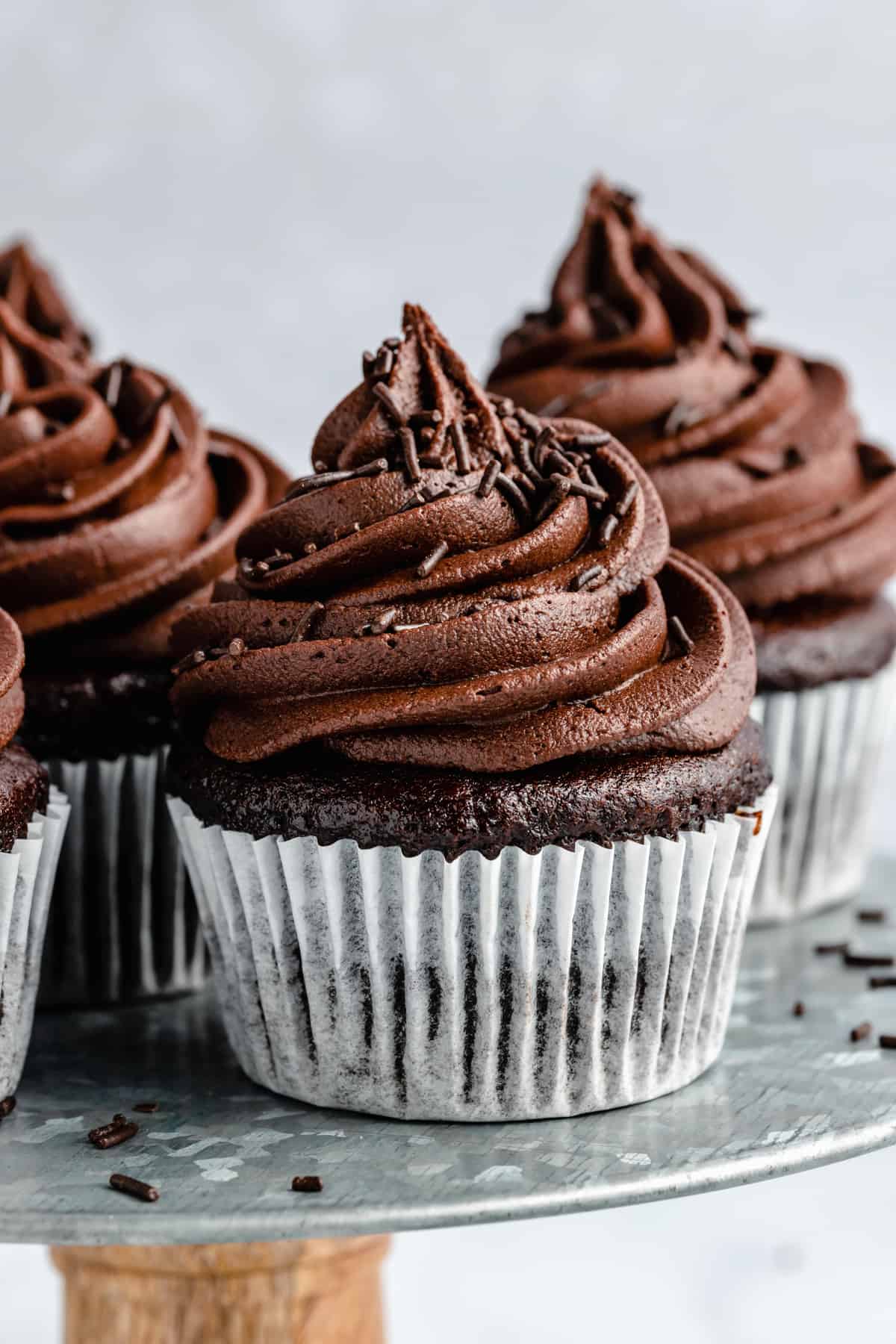 close up of frosted vegan chocolate cupcakes on a metal cake stand