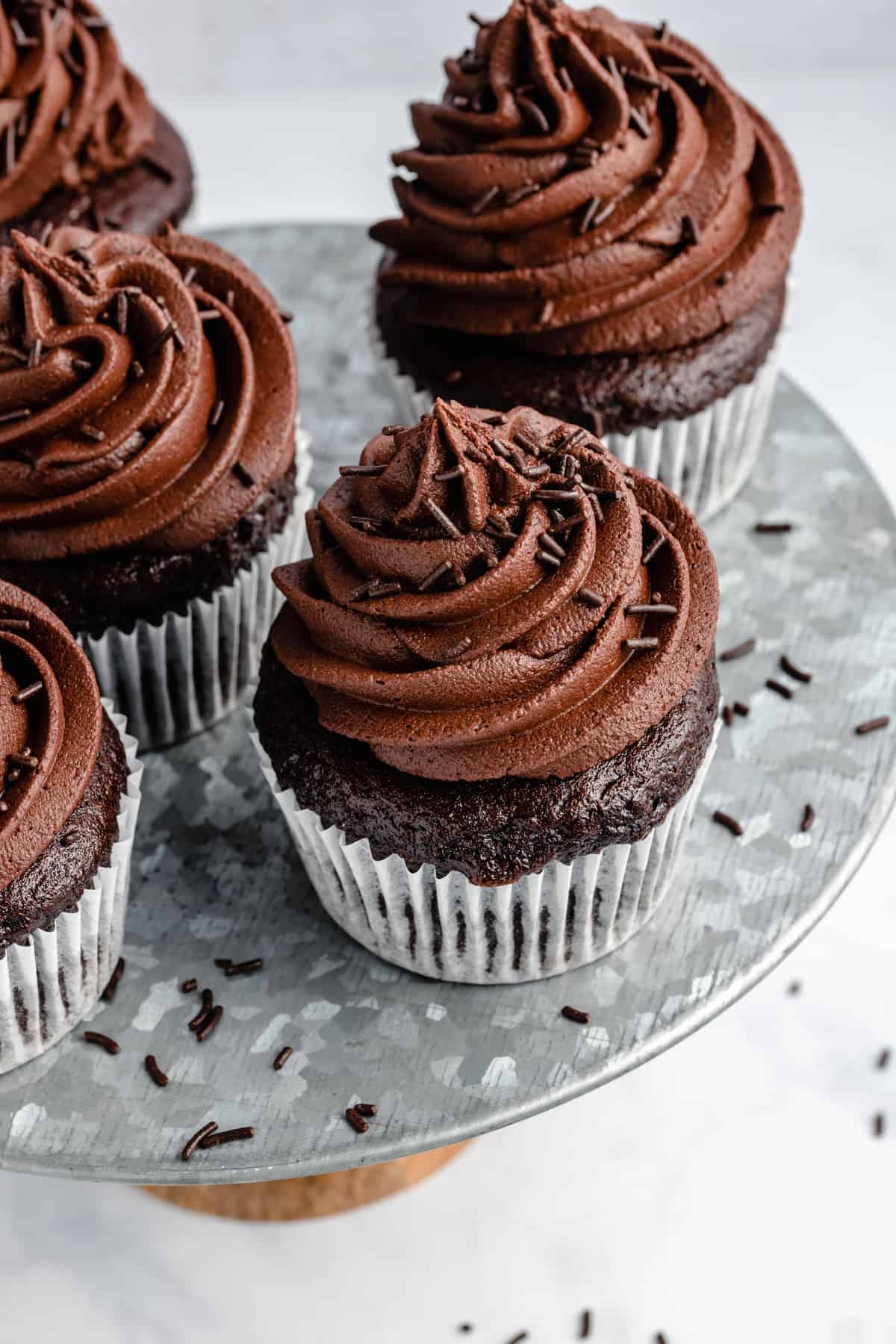 five chocolate cupcakes with frosting on a metal cake stand