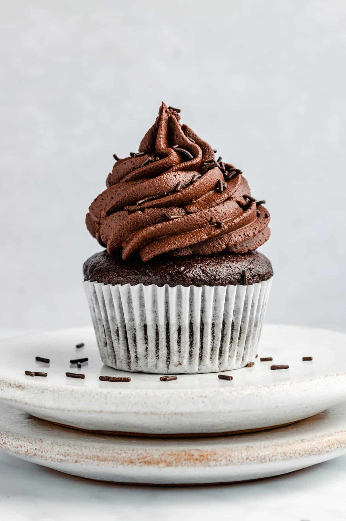 a single vegan chocolate cupcake with frosting on two stacked plates