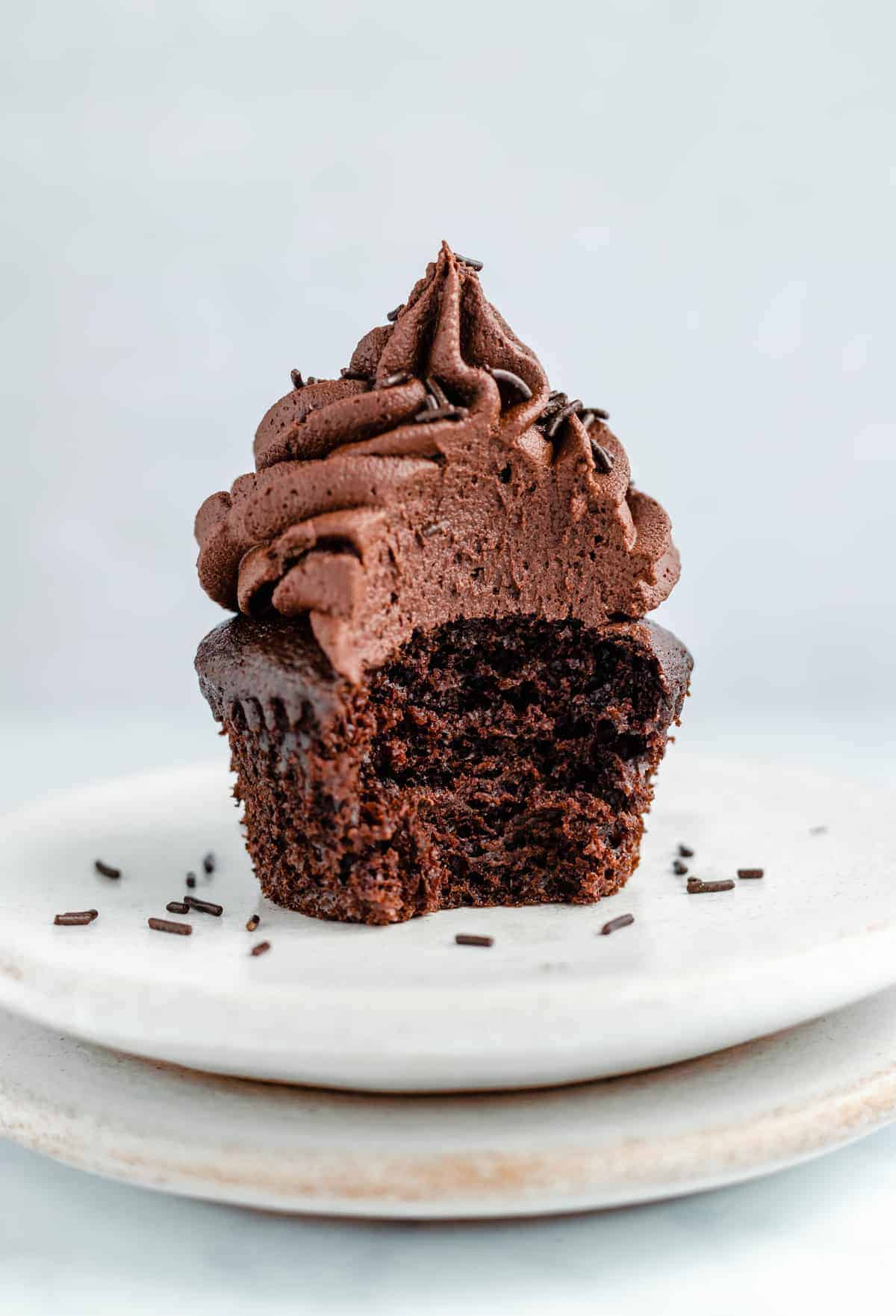 single chocolate cupcake with frosting on a plate with a bite taken out of it