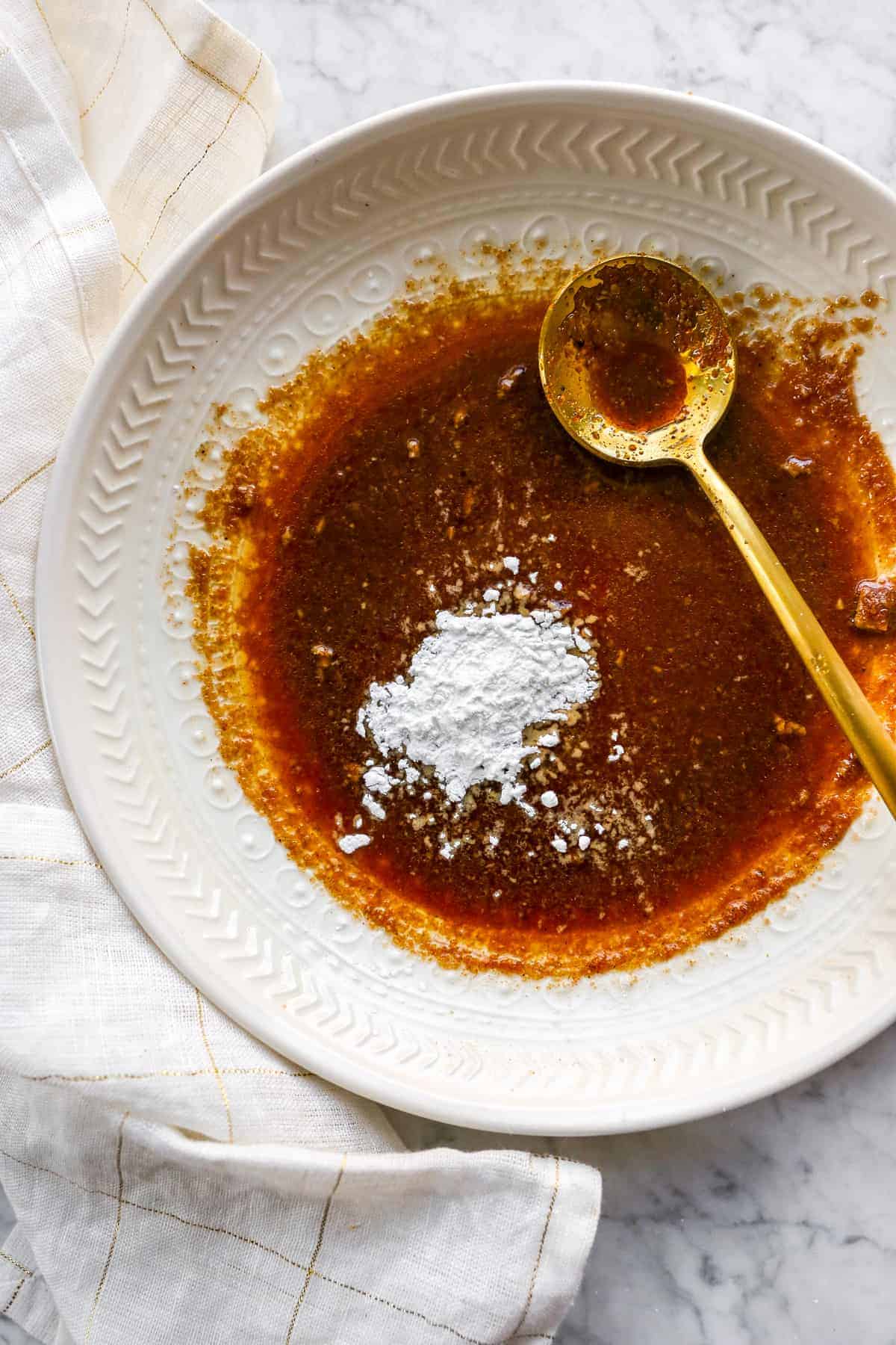 cornstarch in a bowl of leftover marinade with a gold spoon