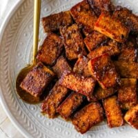 marinated and cooked tofu on a plate with a gold spoon holding some tofu