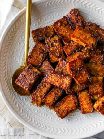 marinated and cooked tofu on a plate with a gold spoon holding some tofu