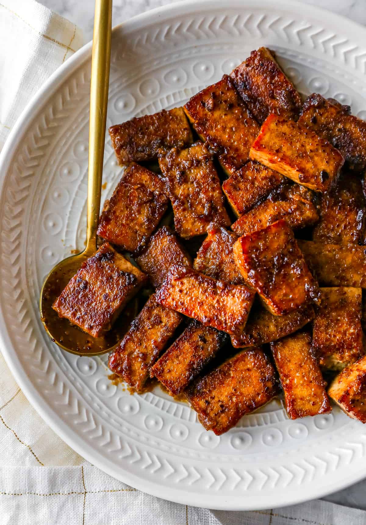 marinated and cooked tofu on a plate with a gold spoon holding some tofu