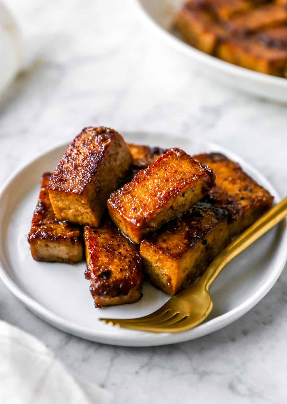 marinated and cooked tofu on a plate with a gold fork 