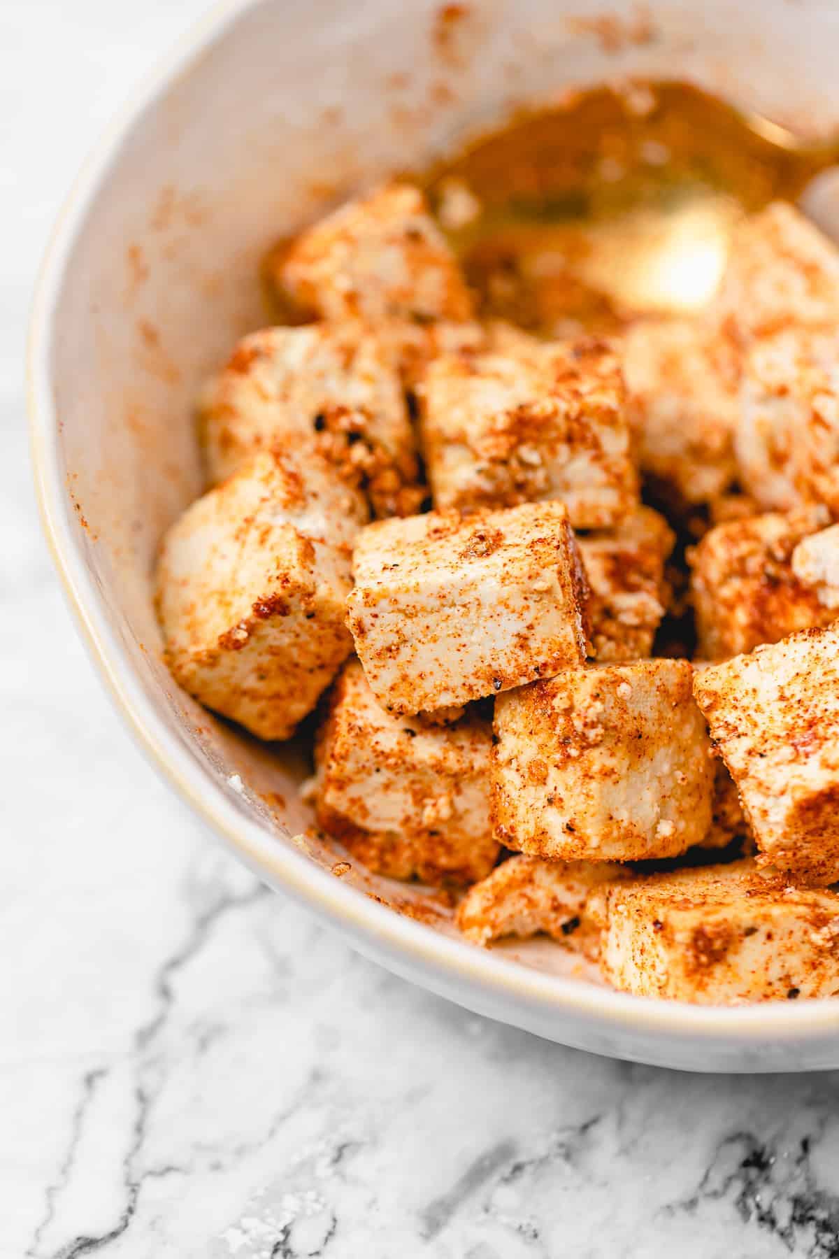 Seasoned raw tofu marinating in a white bowl with a gold spoon