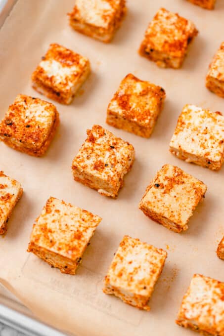 Cubes of uncooked firm tofu covered in seasoning on parchment paper