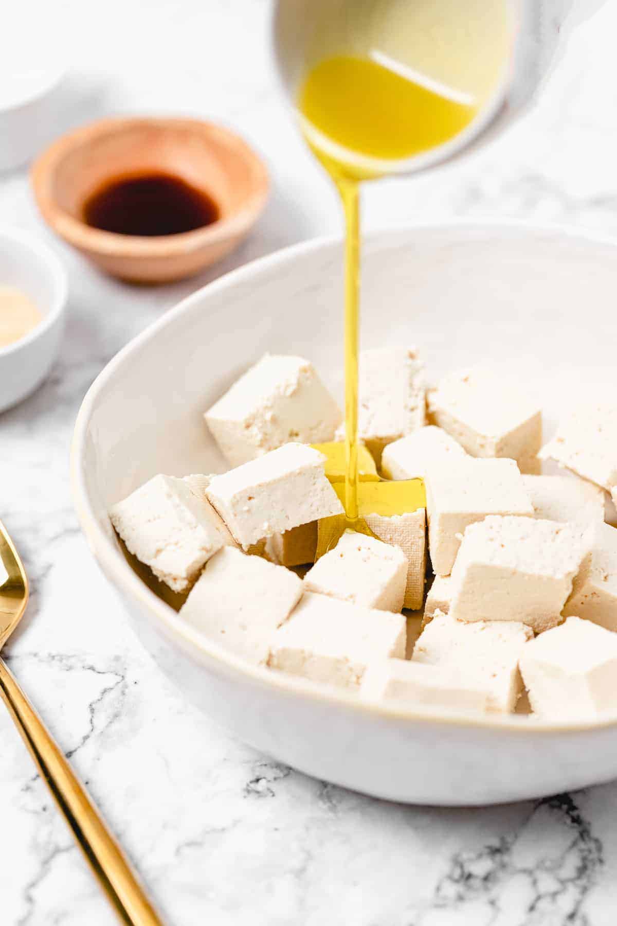 Olive oil poured over a white bowl of tofu chunks
