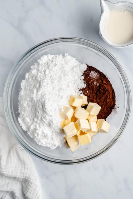 Powdered sugar, butter, and cocoa powder in a glass mixing bowl