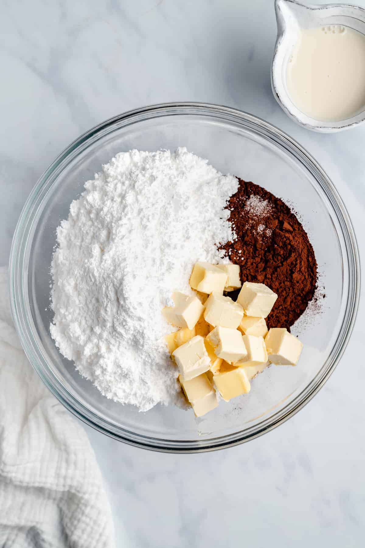 Powdered sugar, butter, and cocoa powder in a glass mixing bowl