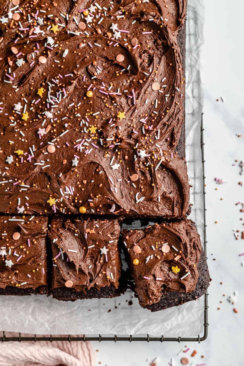 Chocolate sheet cake covered in creamy chocolate frosting with sprinkles on a cooling rack