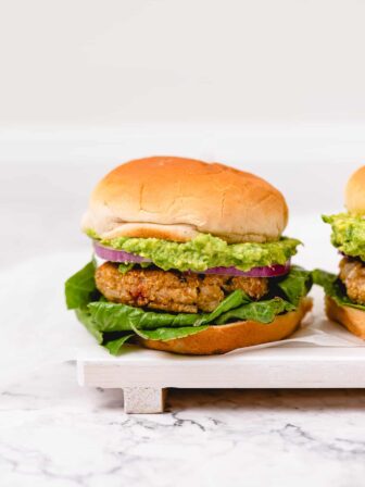 Two golden brown veggie burgers with avocado, red onion, and lettuce on fluffy vegan buns