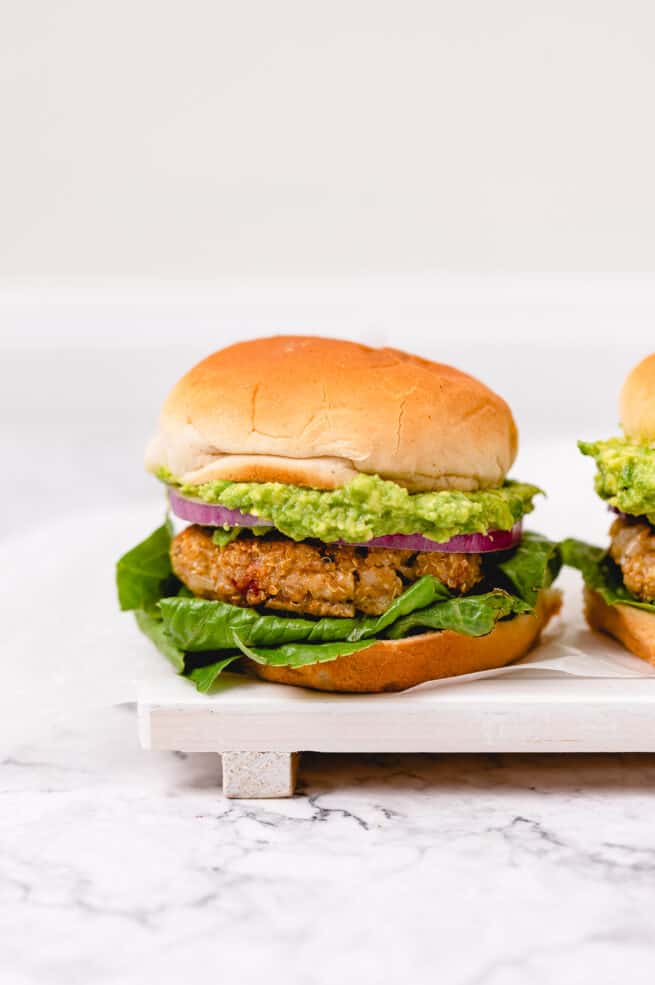 Two golden brown veggie burgers with avocado, red onion, and lettuce on fluffy vegan buns