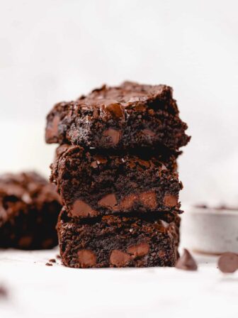 three brownies stacked on top of one another with one in the corner and a bowl of chocolate chips