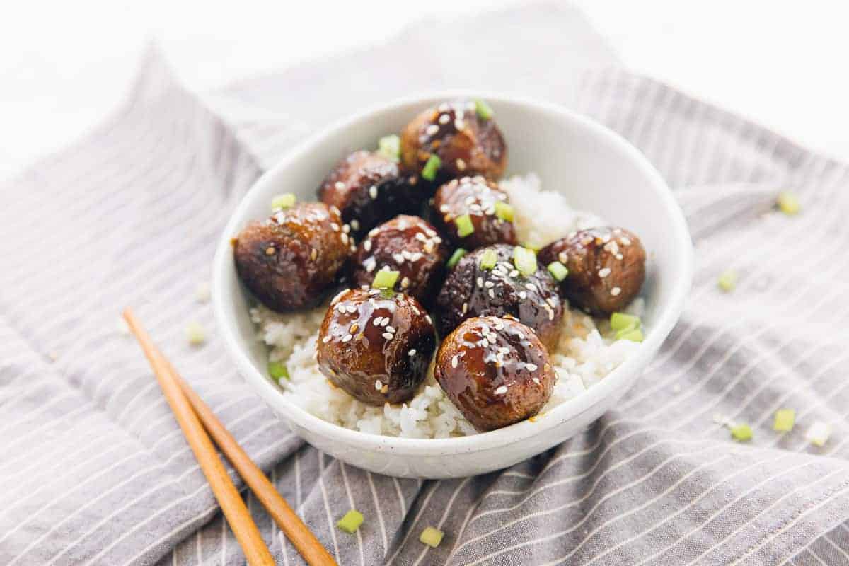 A white bowl of vegetarian meatballs on a bed of white rice with a brown sticky sauce
