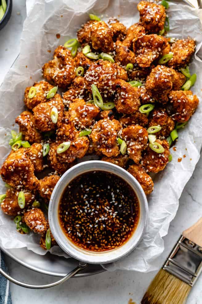 plate of cauliflower wings in a tray with sauce in a small bowl beside it