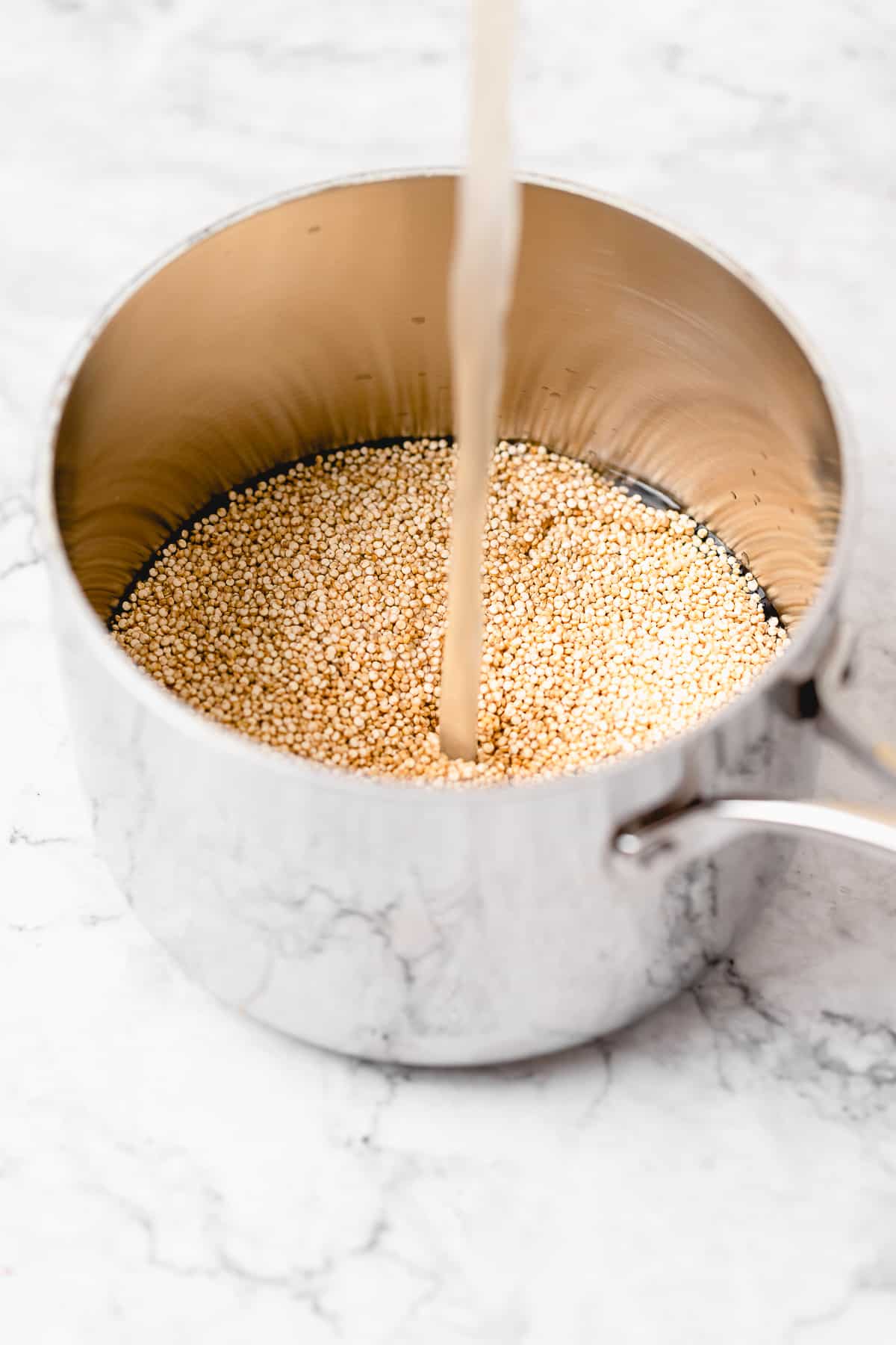 dry quinoa in a measuring cup with veggie broth being poured in