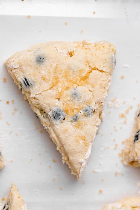 a close up of an unbaked scone piece with coarse sugar sprinkled over