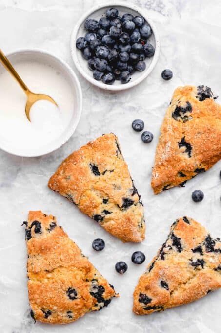 baked blueberry scones with a bowl of lemon glaze and blueberries