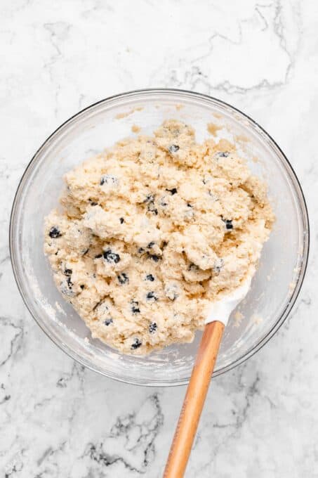 spatula in a bowl of blueberries mixed into scone dough