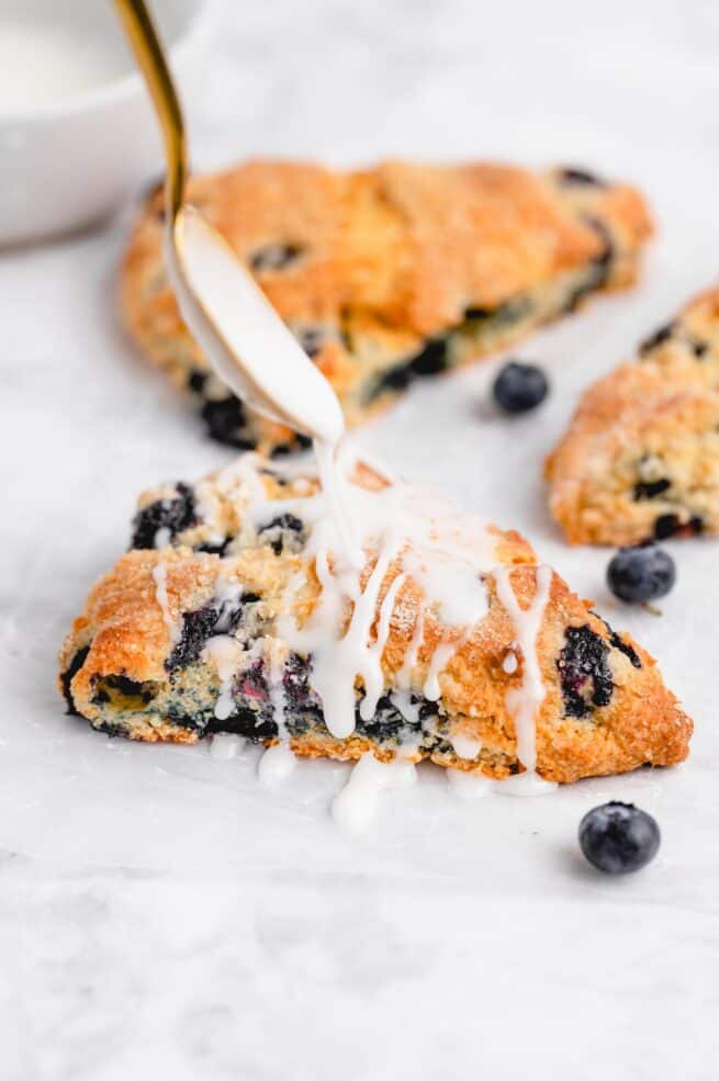 white glaze being drizzled onto a blueberry scone