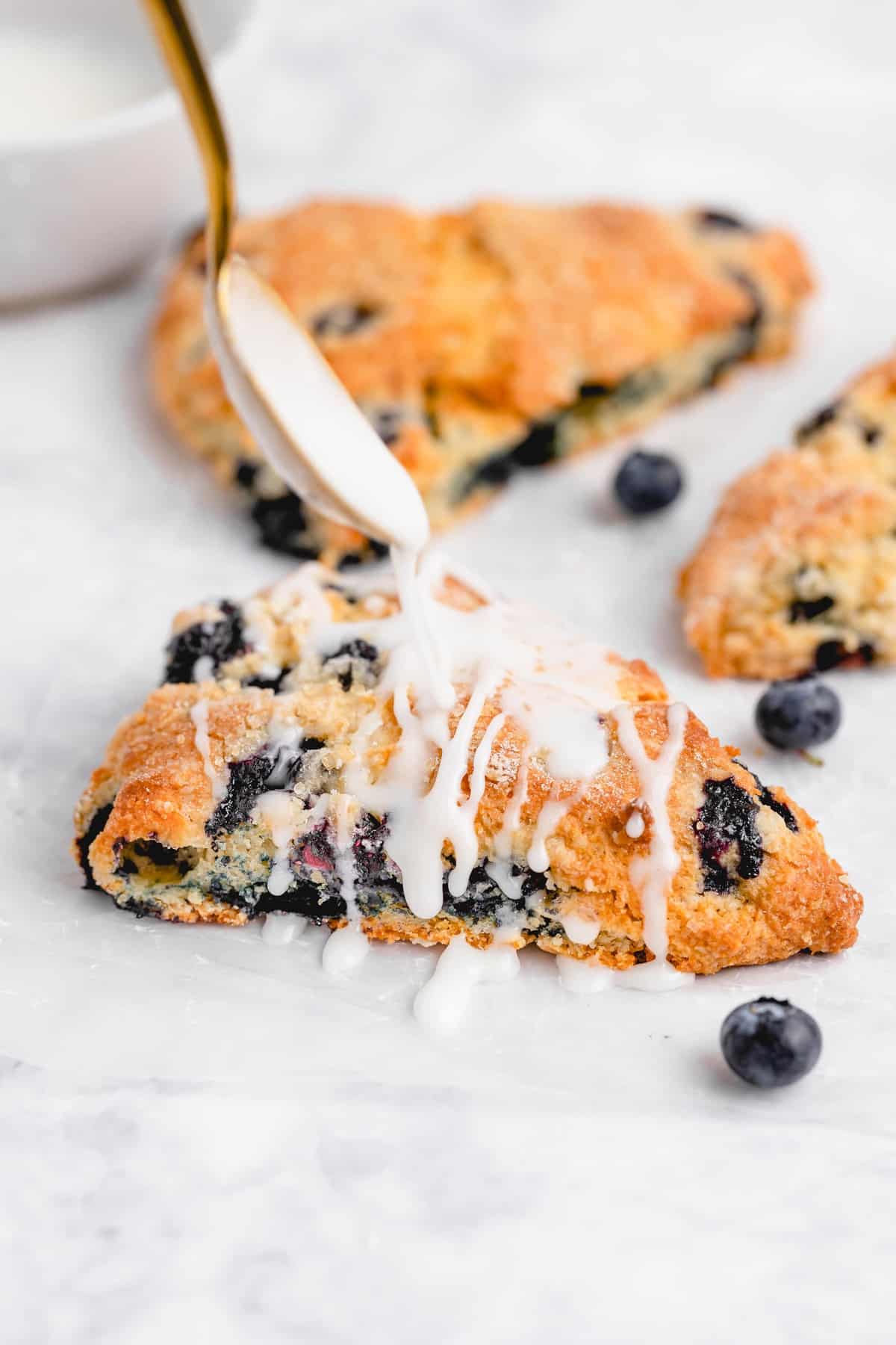 white glaze being drizzled onto a blueberry scone