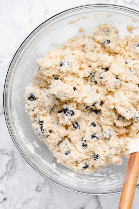 spatula in a bowl of blueberries mixed into scone dough