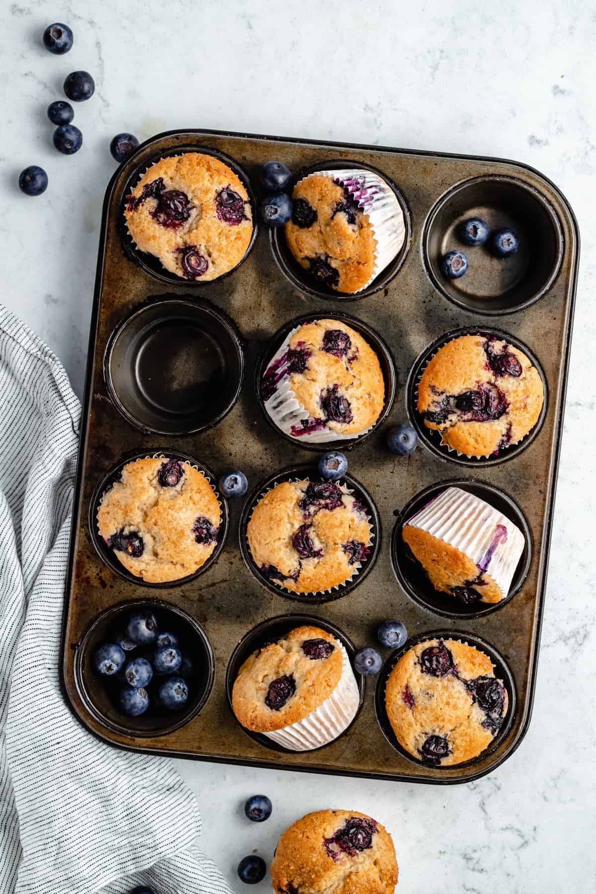 Blueberry muffins and blueberries in a muffin pan.