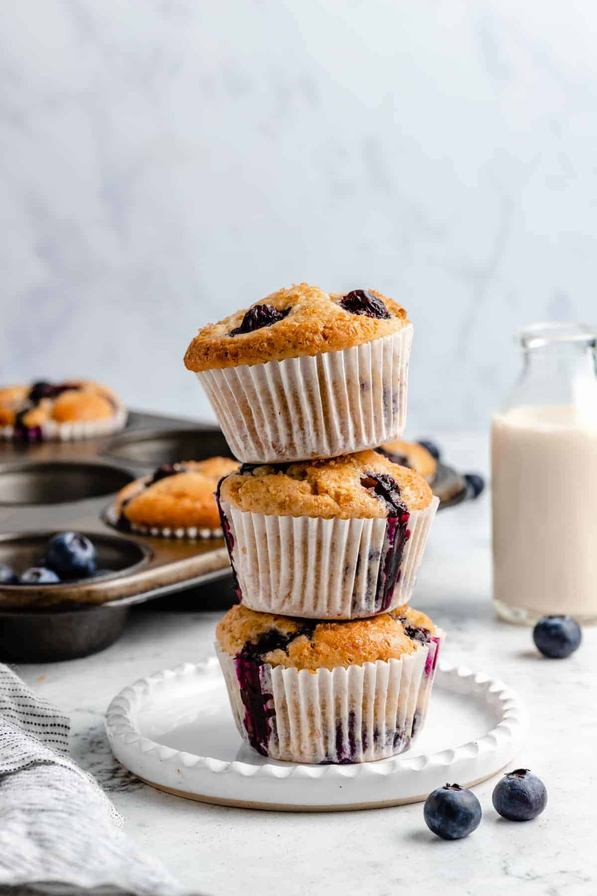 Three stacked blueberry muffins on a plate.