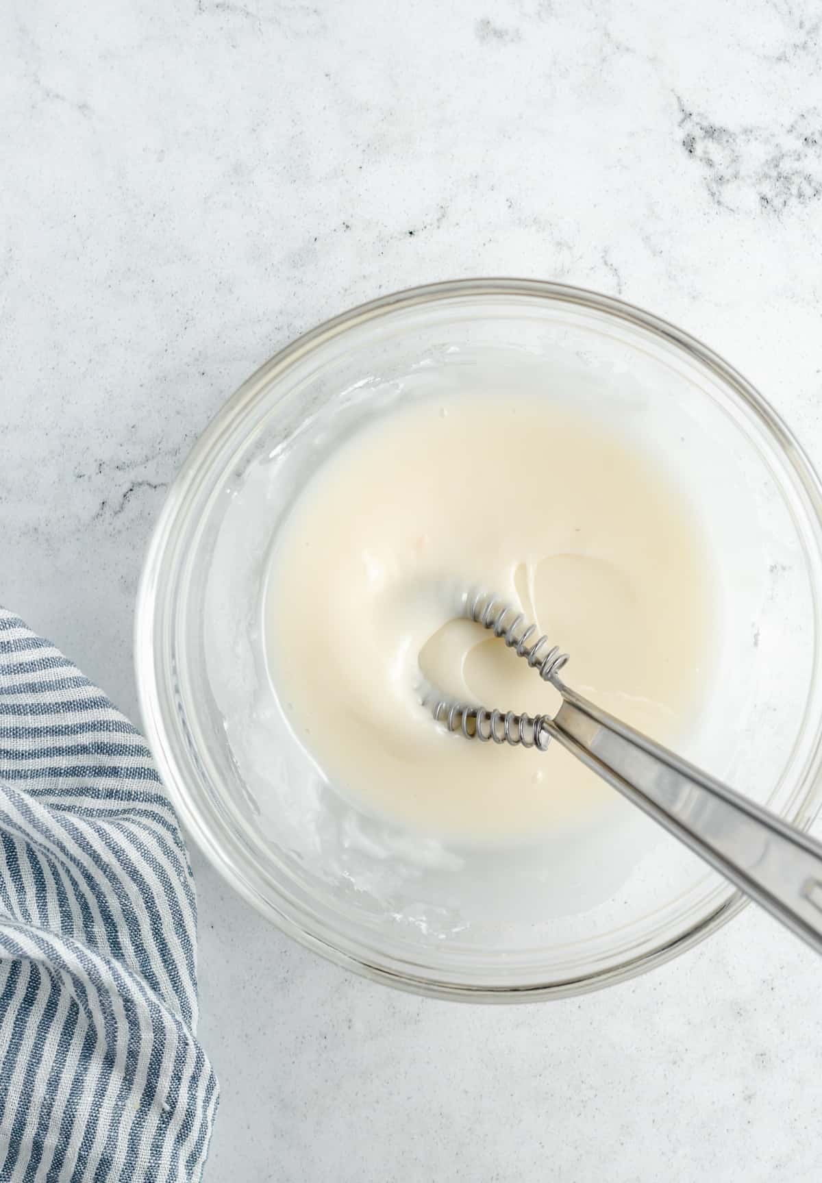 This sweet glazed lemon loaf is part quick bread, part cake! It's soft and moist, made with real lemon zest and juice, without eggs or dairy. Lemon-vanilla glaze in a mixing bowl.